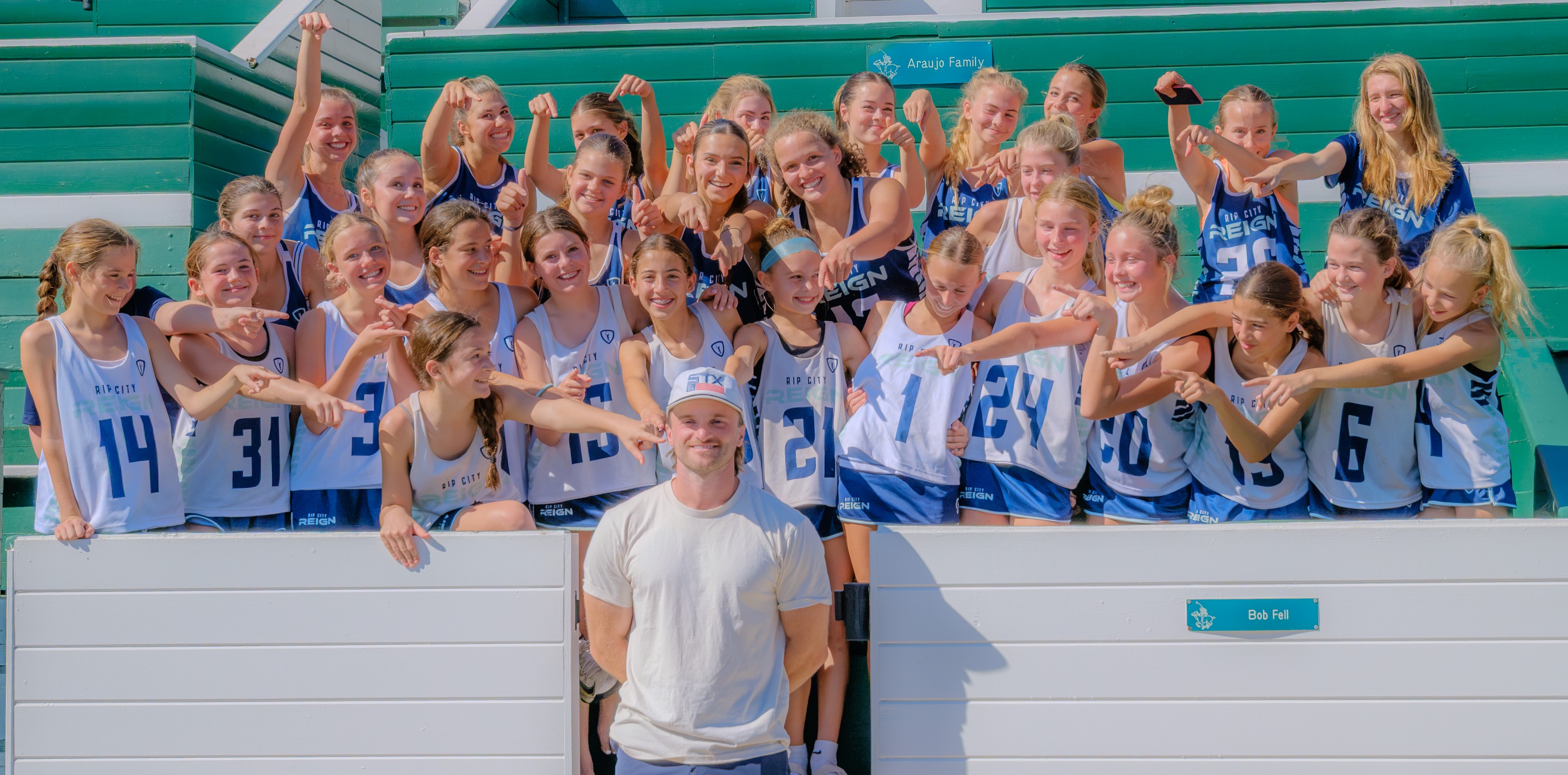 Reign’s 2029 and 2032 teams smiling and flexing together in the bleachers at Santa Barbara Showdown
